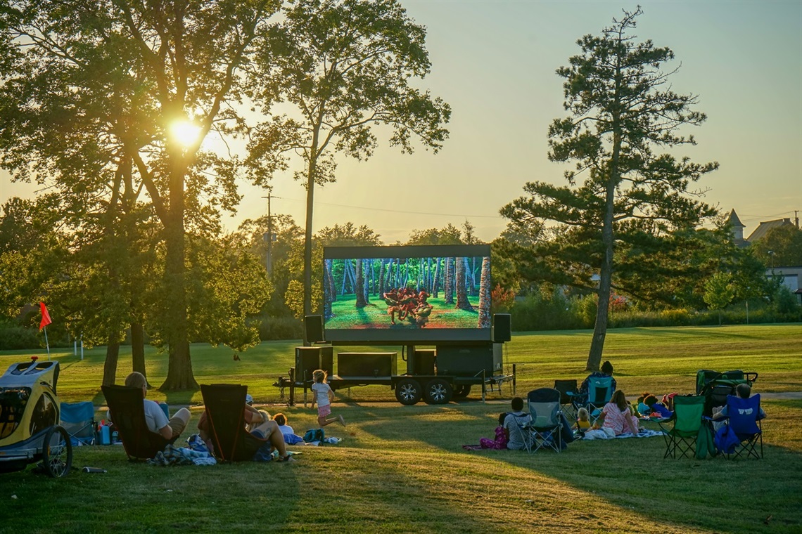 Summer Cinema event attendees watching a movie on a large digital screen in Upjohn Park as the sun sets. 