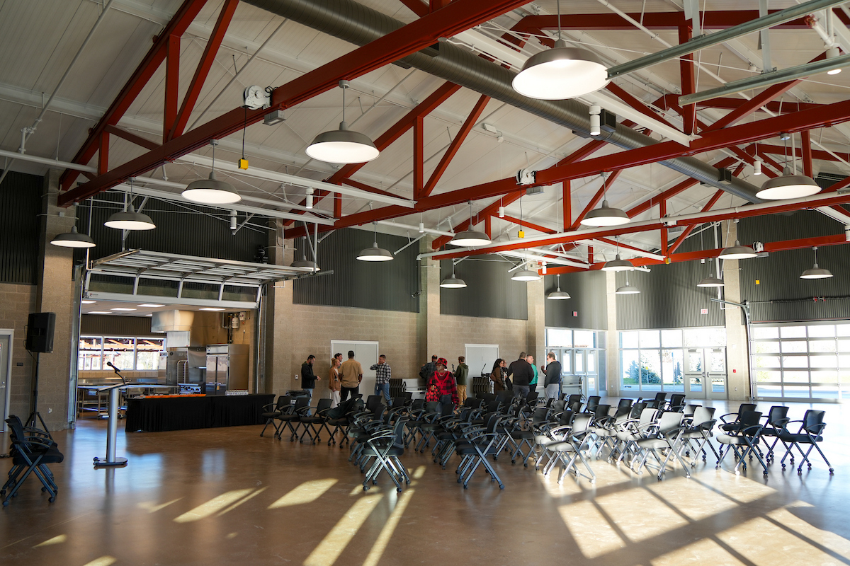 A photo of the interior of the Don Cooney Cultivation Center. A large room with high ceilings setup for an event with chairs, with a kitchen and people in the background.