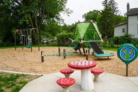 A photo of a play structure, swing set, and mushroom tables and stools.
