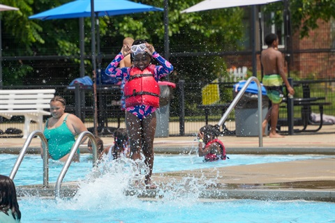 Photo of a splash at Kik Pool and girl standing next to pool smiling and putting on goggles. 